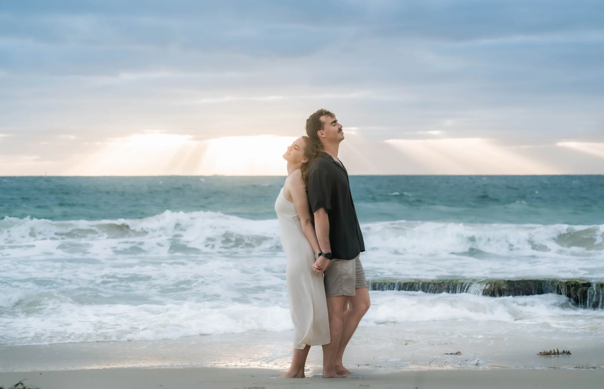 Marcja and Henrico holding hands beneath sun rays at Cottesloe Beach